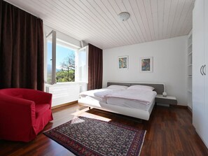 A bedroom with a bed, a red chair, a rug, and two paintings on the wall. - Haus Stirnemann/ Wohnung H-3 by Interhome (Weggis)