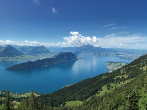 Une vue panoramique d’un paysage montagneux avec un grand lac, entouré de zones boisées et de montagnes lointaines.