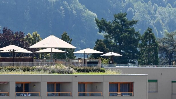 A hotel with multiple rooms, outdoor umbrellas, and a forested mountain backdrop. - Appartement Alpenblick / G6 by Interhome (Weggis)