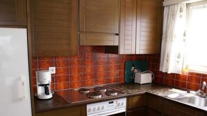 A kitchen with wooden cabinets, a stove, a coffee maker, and a window with curtains. - Appartement Alpenblick / C1 by Interhome (Weggis)