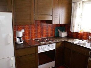 A kitchen with wooden cabinets, a stove, a coffee maker, and a window with curtains. - Appartement Alpenblick / C1 by Interhome (Weggis)