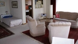 A living room with a bed, two armchairs, a sofa, a coffee table, and a red rug. There is a painting on the wall and a window with curtains. - Appartement Alpenblick / C1 by Interhome (Weggis)