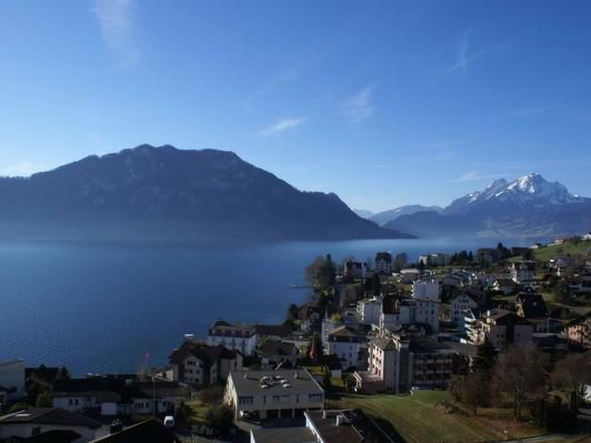 Une ville au bord d’un lac, avec des bâtiments, une montagne et un ciel dégagé.