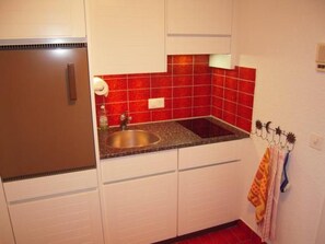 A kitchen with white cabinets, a stainless steel sink, red tiles, and a towel rack with towels. - Appartement Alpenblick / 02 by Interhome (Weggis)