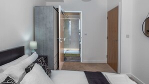 A modern bedroom with a large bed, a bedside table with a lamp, a wardrobe, and a door leading to a bathroom with a shower and a toilet. - Brandneue, zentrale 2-Zimmer-Wohnung für 6 Gäste by Interhome (Preston)