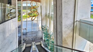 A modern interior with a wooden slatted ceiling, marble walls, and an escalator leading to a glass entrance. - Manoré By SanLiving - 2BR - Private Lift (Jakarta)