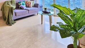 A modern living room with a sofa, a coffee table, and a large window with a city view. - Manoré By SanLiving - 2BR - Private Lift (Jakarta)