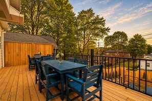 Um deck de madeira com mesa e cadeiras, cercado por um muro de madeira e árvores.