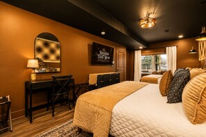 Quarto de hotel com uma cama grande, uma escrivaninha, uma cadeira, um espelho, uma placa emoldurada e uma janela com cortinas.