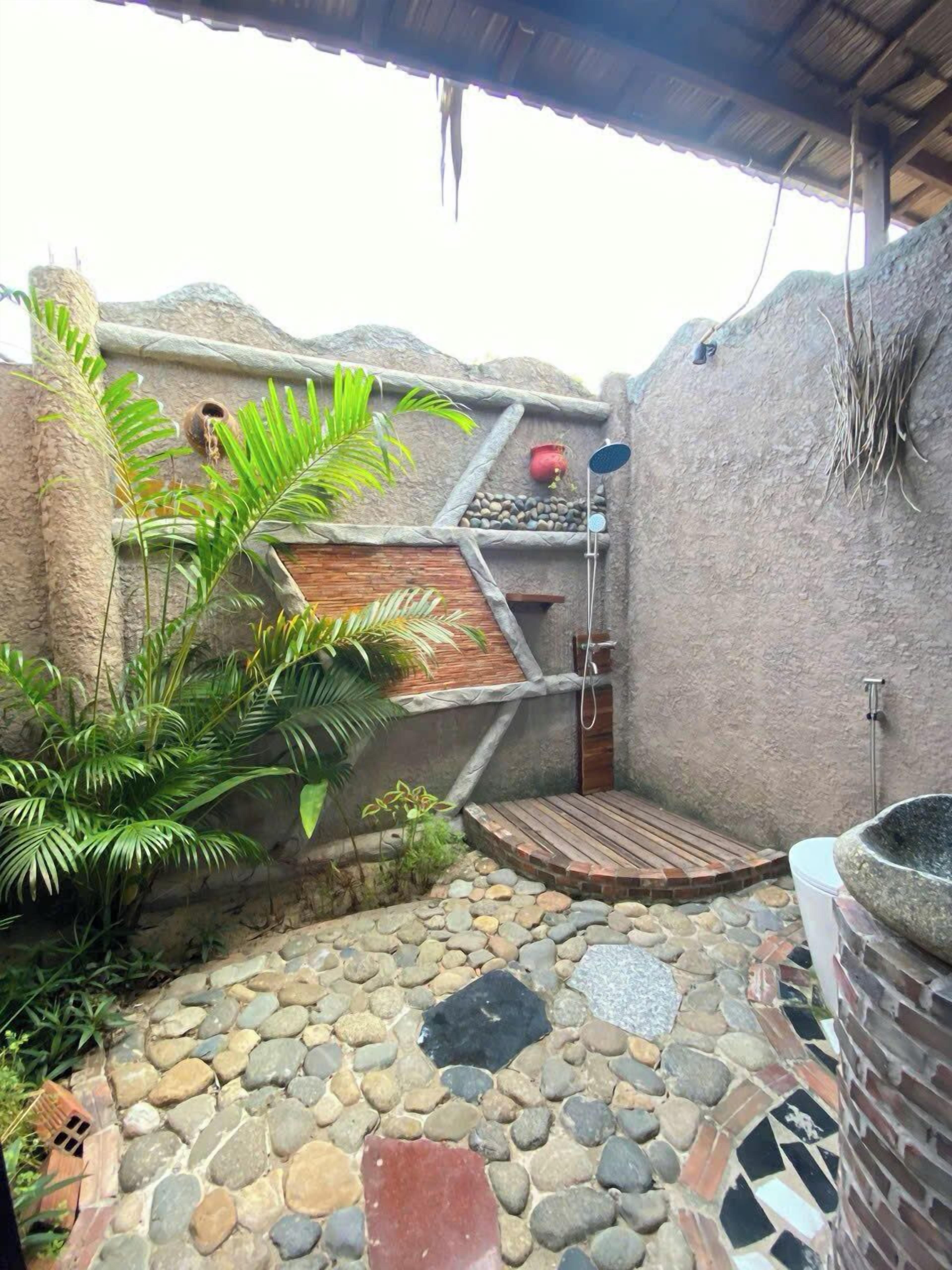 A stone-tiled patio with a wooden deck, a small waterfall feature, and a rustic stone wall.