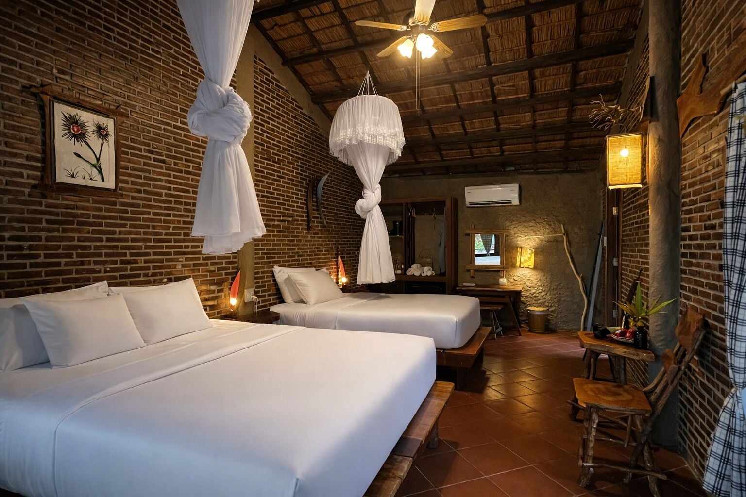 A room with two beds, a ceiling fan, a brick wall, and a wooden floor.