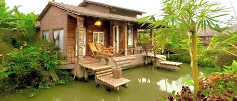 A rustic wooden house with a porch, a small pool, and lush greenery surrounding it.