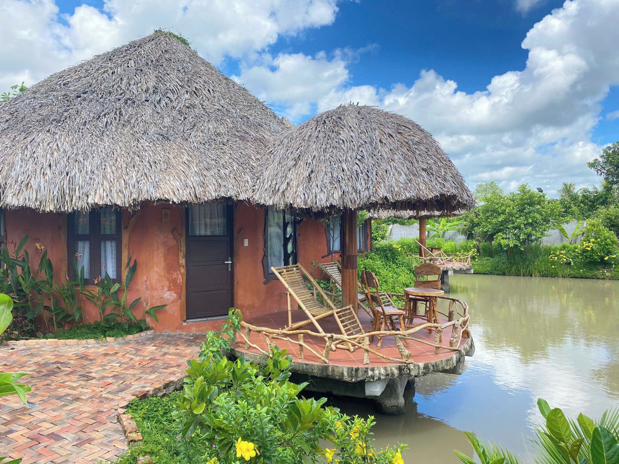 A thatched-roof bungalow with a dock extending into a calm body of water, surrounded by lush greenery.