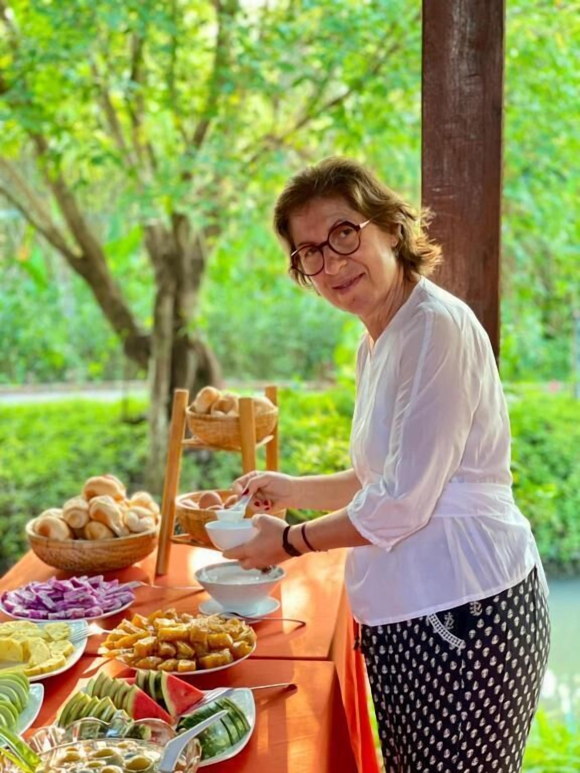 Una persona sirviendo comida en una mesa al aire libre, con varios platos y pan.