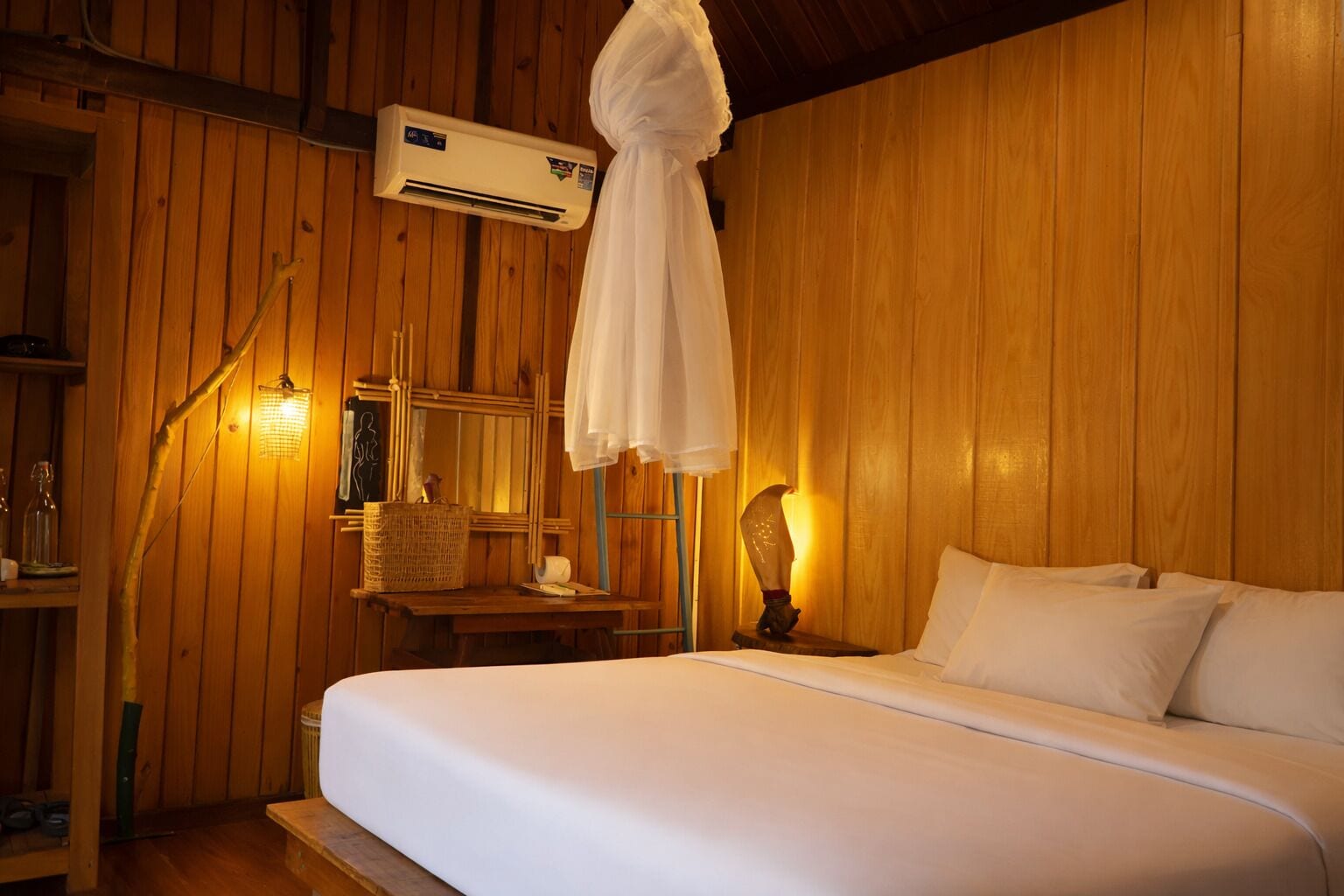 A wooden room with a bed, a nightstand, a wall-mounted air conditioner, and a hanging mosquito net.