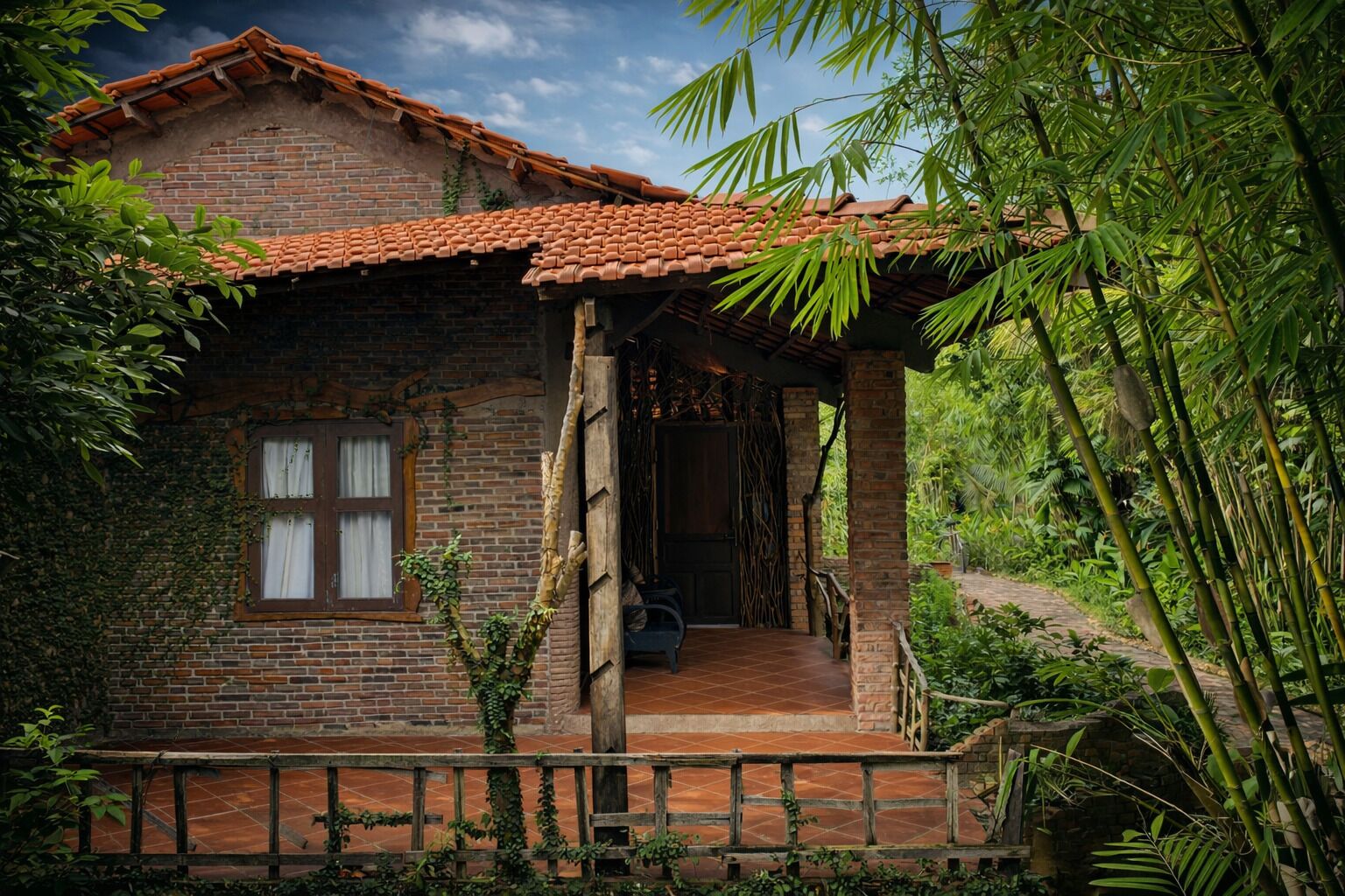 Une maison de campagne en briques, avec un toit en tuiles, un porche en bois et un chemin en briques menant à l’entrée.