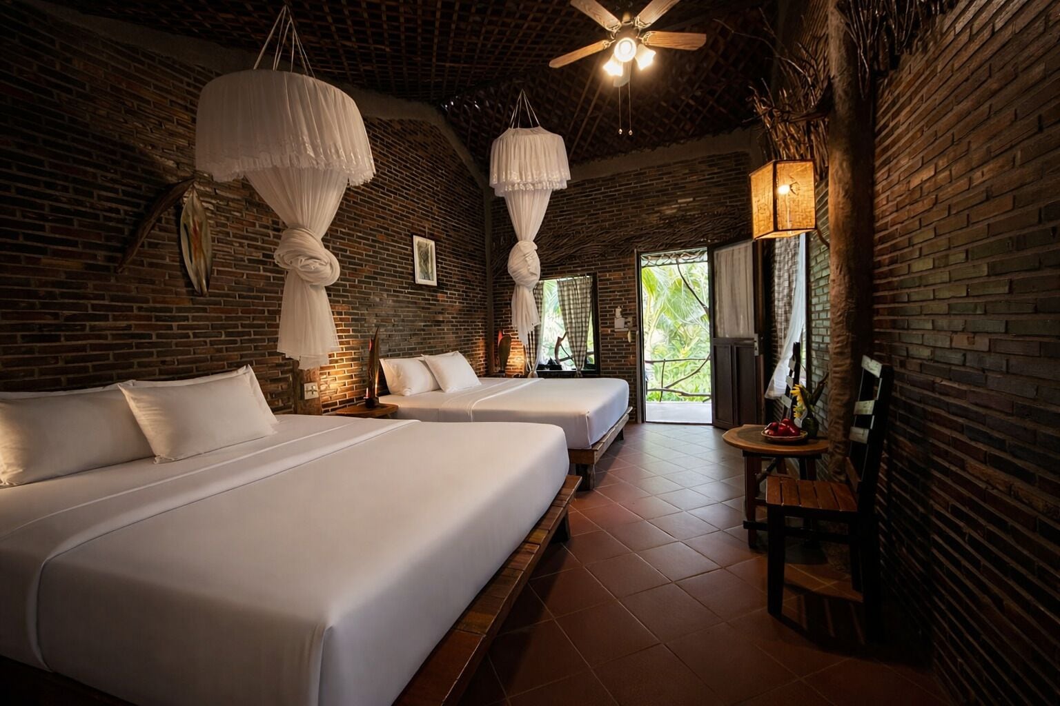 A hotel room with two beds, a ceiling fan, and a view of greenery outside.
