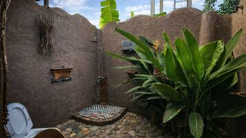 Une salle de bain rustique avec une douche, une petite étagère en bois et des toilettes.