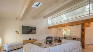Ein geräumiger Wohnbereich mit hohen Decken, einem großen Flachbildfernseher, einem Essbereich und Blick ins Freie durch Dachfenster.