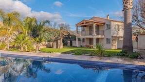 Ein zweistöckiges Haus mit Pool, umgeben von Palmen und Grünpflanzen.