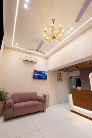 A reception area with a sofa, a TV, a chandelier, and a reception desk. - Lotus Feet Inn (Varanasi)