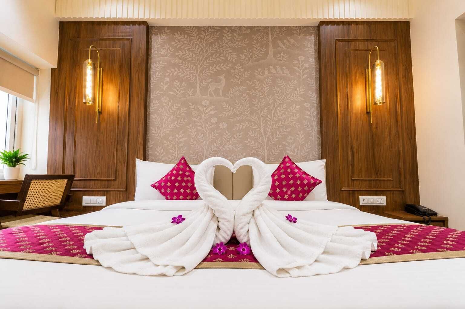 A hotel room with a bed, two wall sconces, a nightstand, and a plant.