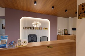 Ein Empfangstresen mit einem Schild, auf dem 'LOTUS FEET INN' und ein 'RECEPTION'-Schild steht. Es gibt Stühle und eine Theke mit Holzoptik.