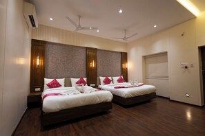 A hotel room with two beds, ceiling fans, a large window, and a wall-mounted air conditioner. - Lotus Feet Inn (Varanasi)