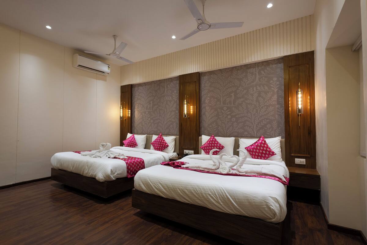 A hotel room with two beds, a ceiling fan, an air conditioning unit, and a patterned wall.