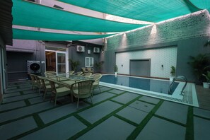 Ein Außenpoolbereich mit Tisch und Stühlen, einer überdachten Terrasse und einer Backsteinmauer.