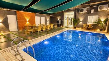Una piscina con borde de azulejos, rodeada de sillones de descanso y un muro de ladrillo.