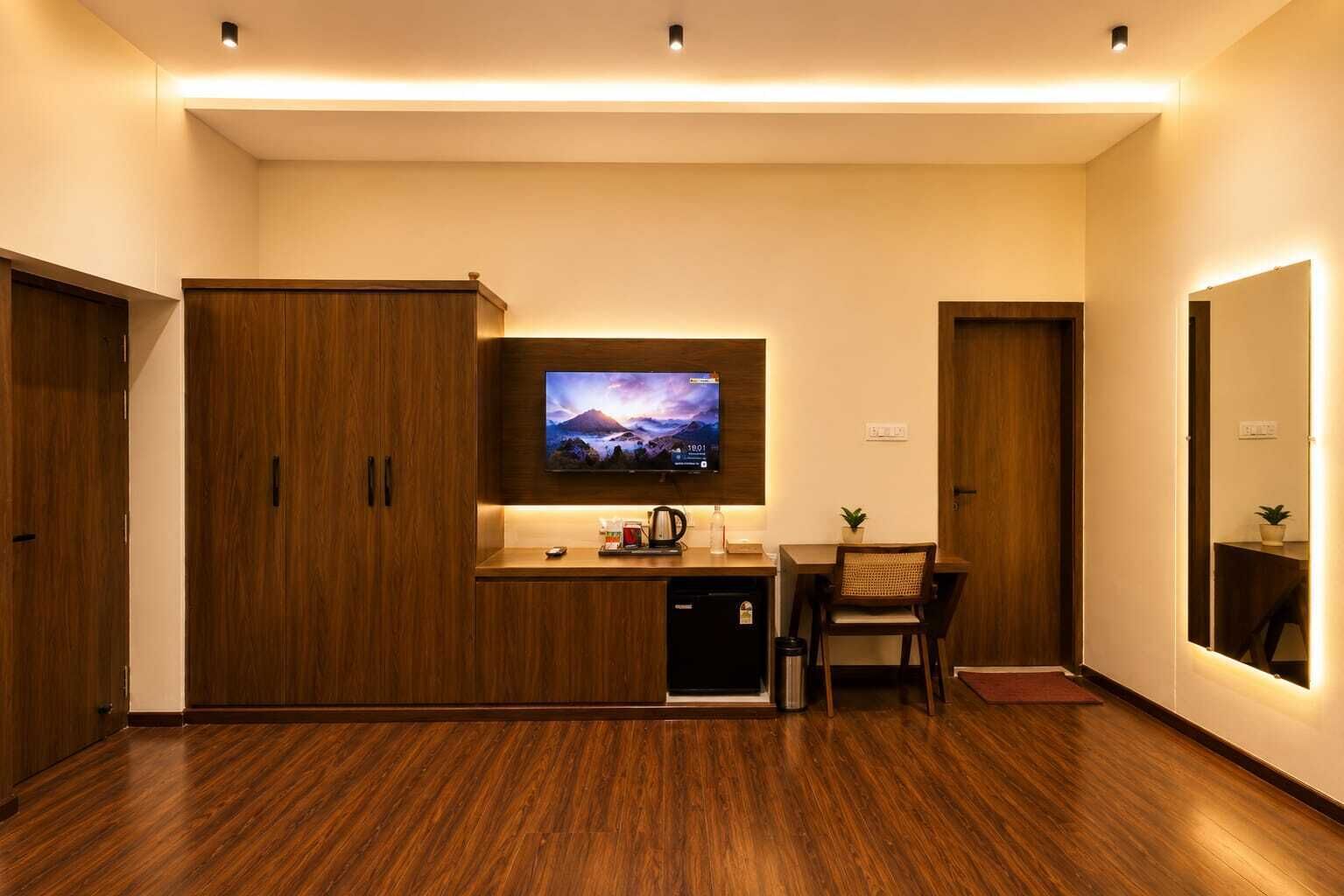 Una habitación de hotel moderna con un armario de madera, un televisor de pantalla plana sobre un escritorio de madera y una pequeña mesa con una silla.