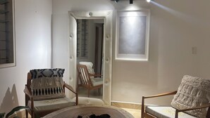 A room with a round wooden table, two upholstered chairs with patterned cushions, a doorway leading to another room, and a wall-mounted light fixture. - Room 202 with air conditioning (Cúcuta)