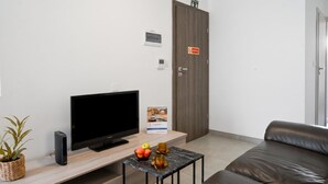 A modern room with a flat-screen TV, a wooden coffee table with fruits and a glass, a leather sofa, and a closed door with a 'No warning' sign. - Camelia Seaview 1 Bd Apart In St Paul Bay (St. Paul's Bay)