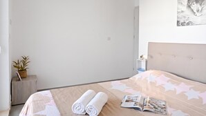A neatly made bed with a patterned bedspread, two rolled towels, and an open magazine on the bed. - Camelia Seaview 1 Bd Apart In St Paul Bay (St. Paul's Bay)