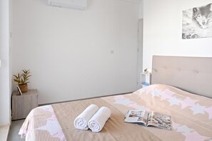 A neatly made bed with a patterned bedspread, two rolled towels, and an open magazine on the bed.