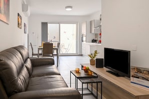 A modern living room with a leather sofa, a flat-screen TV, a small coffee table, and a dining area with a table and chairs.