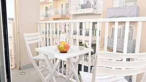 A balcony with white chairs and a table, a bowl of fruit, and a bottle of wine.