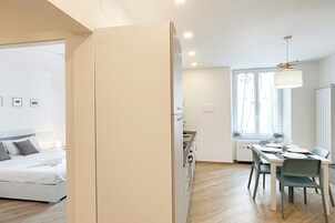 A modern bedroom with a bed, a dining area with a table and chairs, and a kitchen area with cabinets.