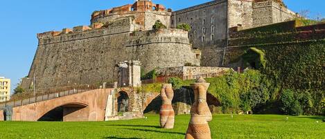 A historic stone fortress with a bridge, terracotta sculptures, and a grassy field.