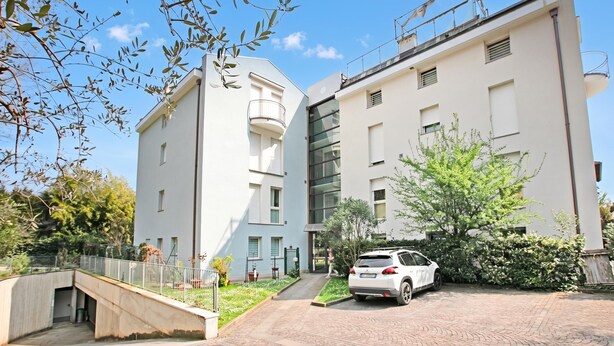 A modern building with a white facade, a covered outdoor area, and a car parked in front. - Appartamento Gioale (Riva del Garda)