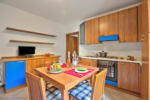 A kitchen with wooden cabinets, a dining table with chairs, a television, and a stove. - Appartamento Gioale (Riva del Garda)