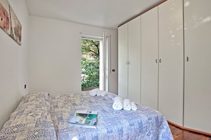 A bedroom with a bed, a wardrobe, and a window with a view of greenery. - Appartamento Gioale (Riva del Garda)