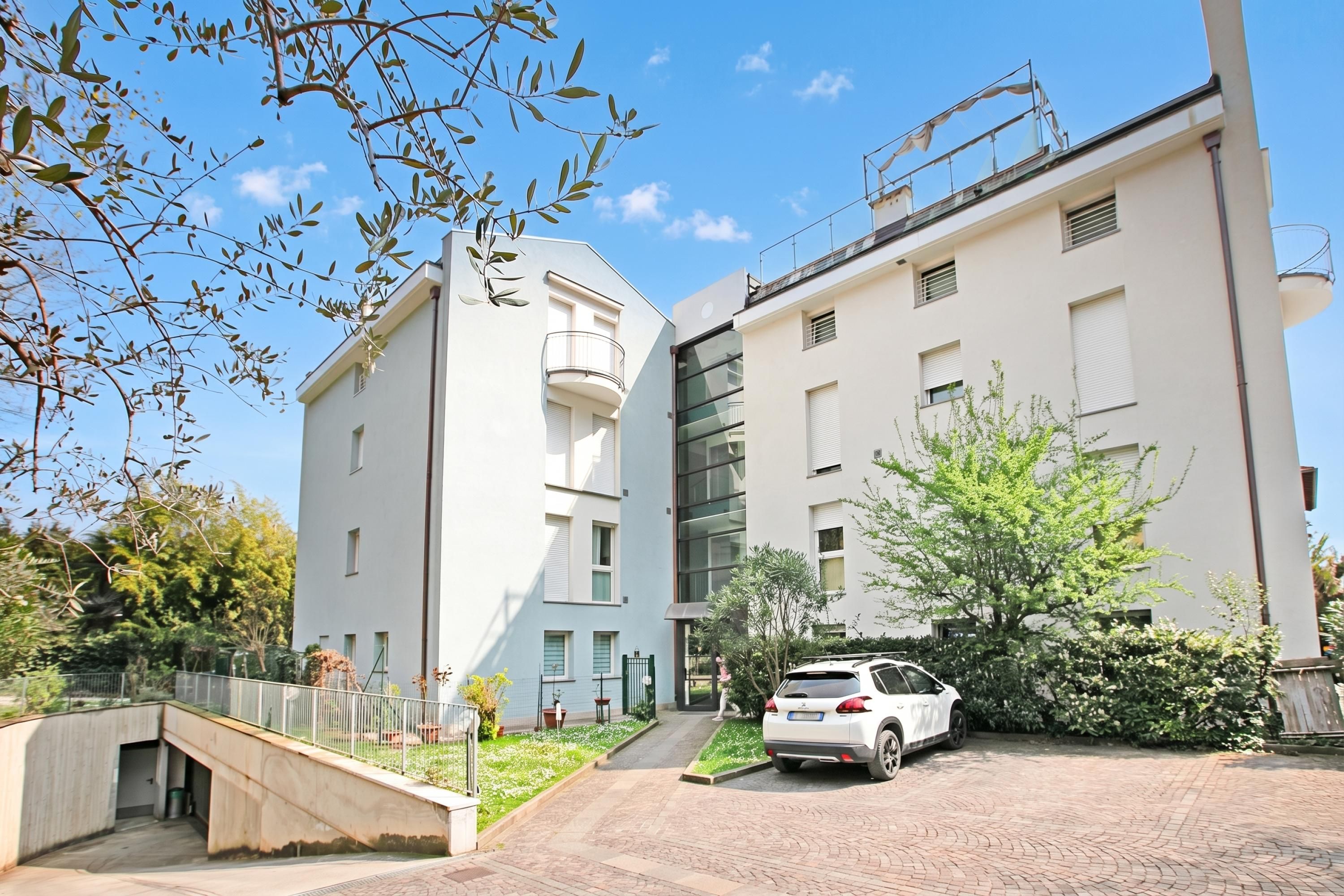 A modern building with a white facade, a covered outdoor area, and a car parked in front.
