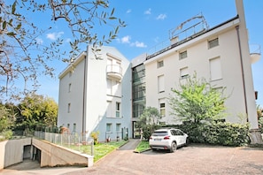 A modern building with a white facade, a covered outdoor area, and a car parked in front. - Appartamento Gioale (Riva del Garda)