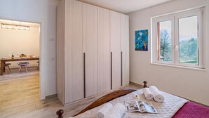 Un dormitorio con cama, armario, ventana con vistas y zona de comedor con mesa y sillas.