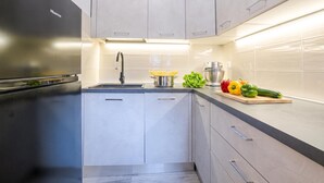 Cocina moderna con refrigerador de acero inoxidable, un lavamanos y una encimera con verduras frescas.