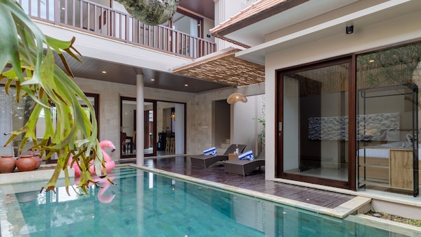 A modern indoor pool area with lounge chairs and a dining area visible in the background. - Villa Amerta by Taman Bali (Ungasan)