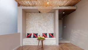 A modern interior with a stone wall, a wooden bench with red and black cushions, and a small round table with two green apples. - Villa Amerta by Taman Bali (Ungasan)