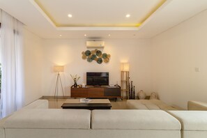 A modern living room with a sofa set, a coffee table, a TV, and decorative wall art. - Villa Amerta by Taman Bali (Ungasan)
